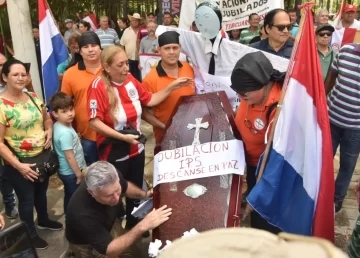 Personas rodeando un cajón funerario que dice "Jubilación IPS Descansen en Paz"