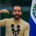 Fotografía de Bukele apuntándose así mismo con una remera beige. De fondo la bandera de El Salvador